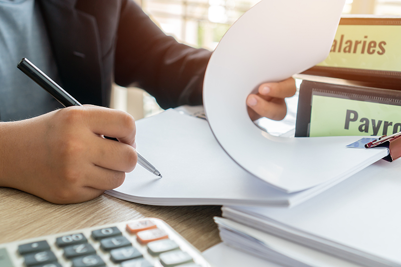 Flipping through paperwork with Salaries and Payroll Binders on desk