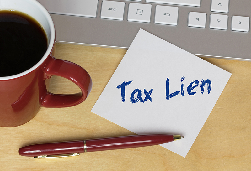 Tax Lien written on a note by a keyboard, cup of coffee, and pen